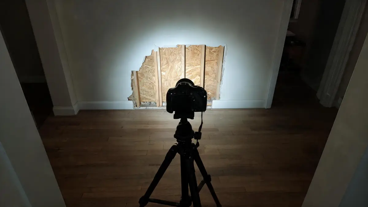 Camera on a tripod documenting a damaged wall