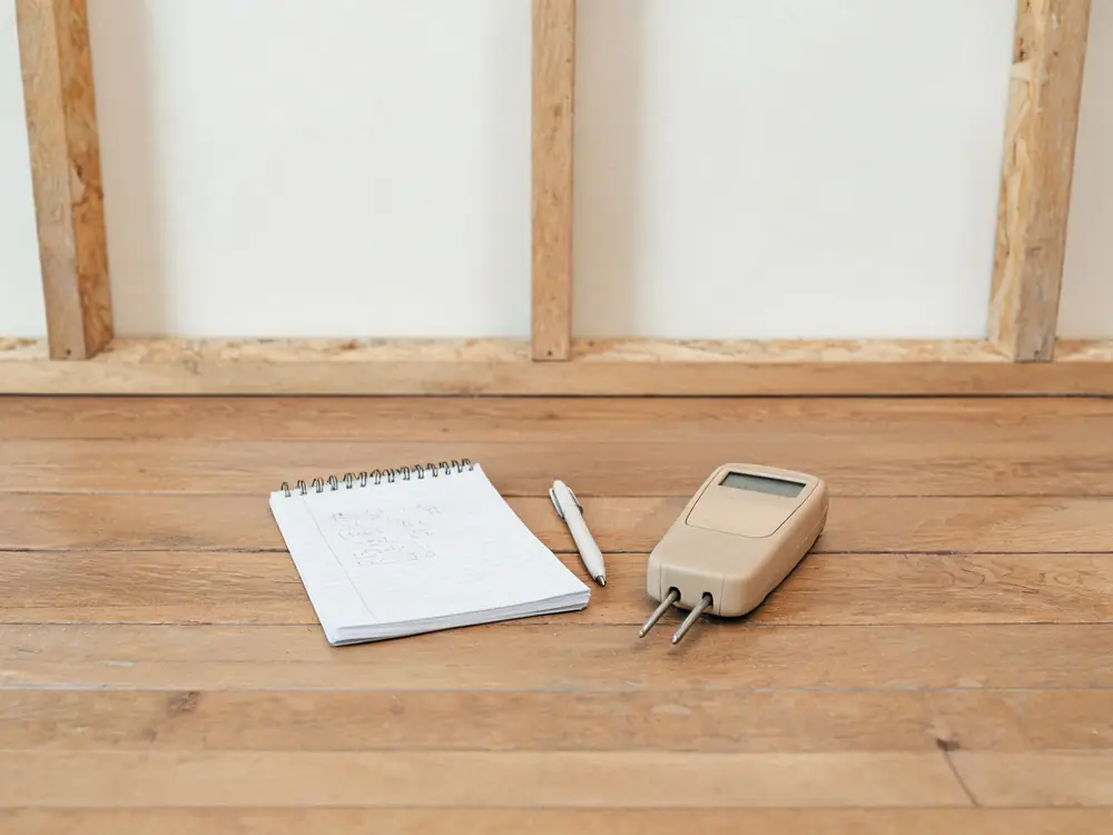 Handwritten moisture log beside a pin-type moisture meter